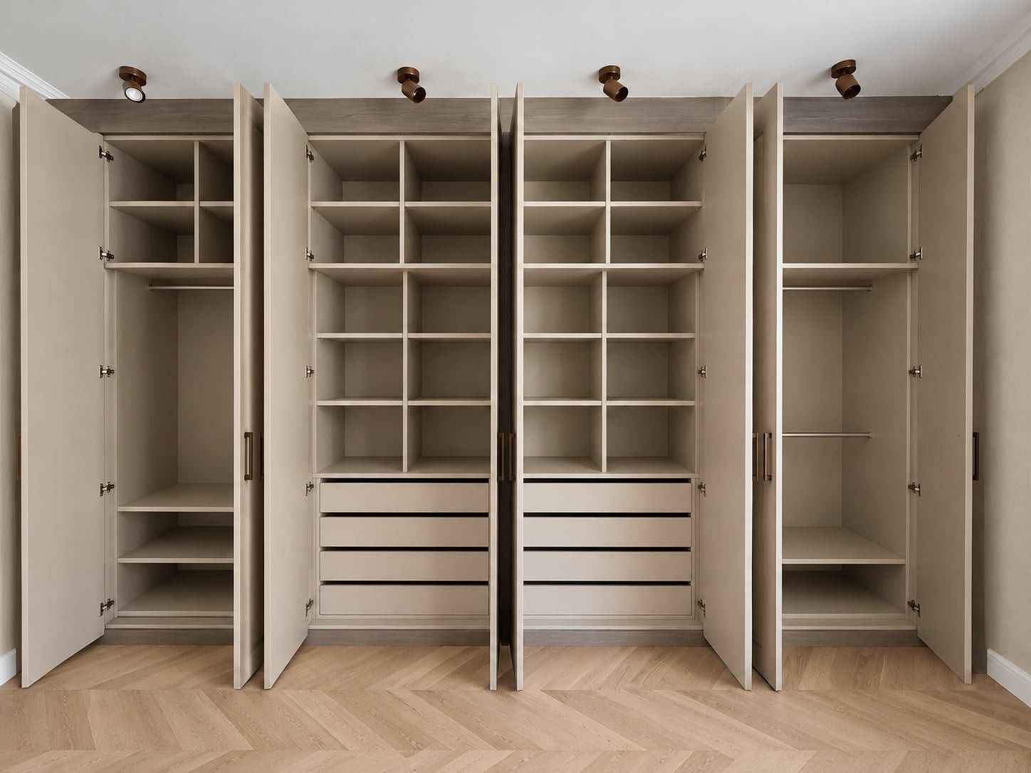 Armoire à quatre corps ouverte : penderies, casiers, étagères et tiroirs, sous des spots bronze