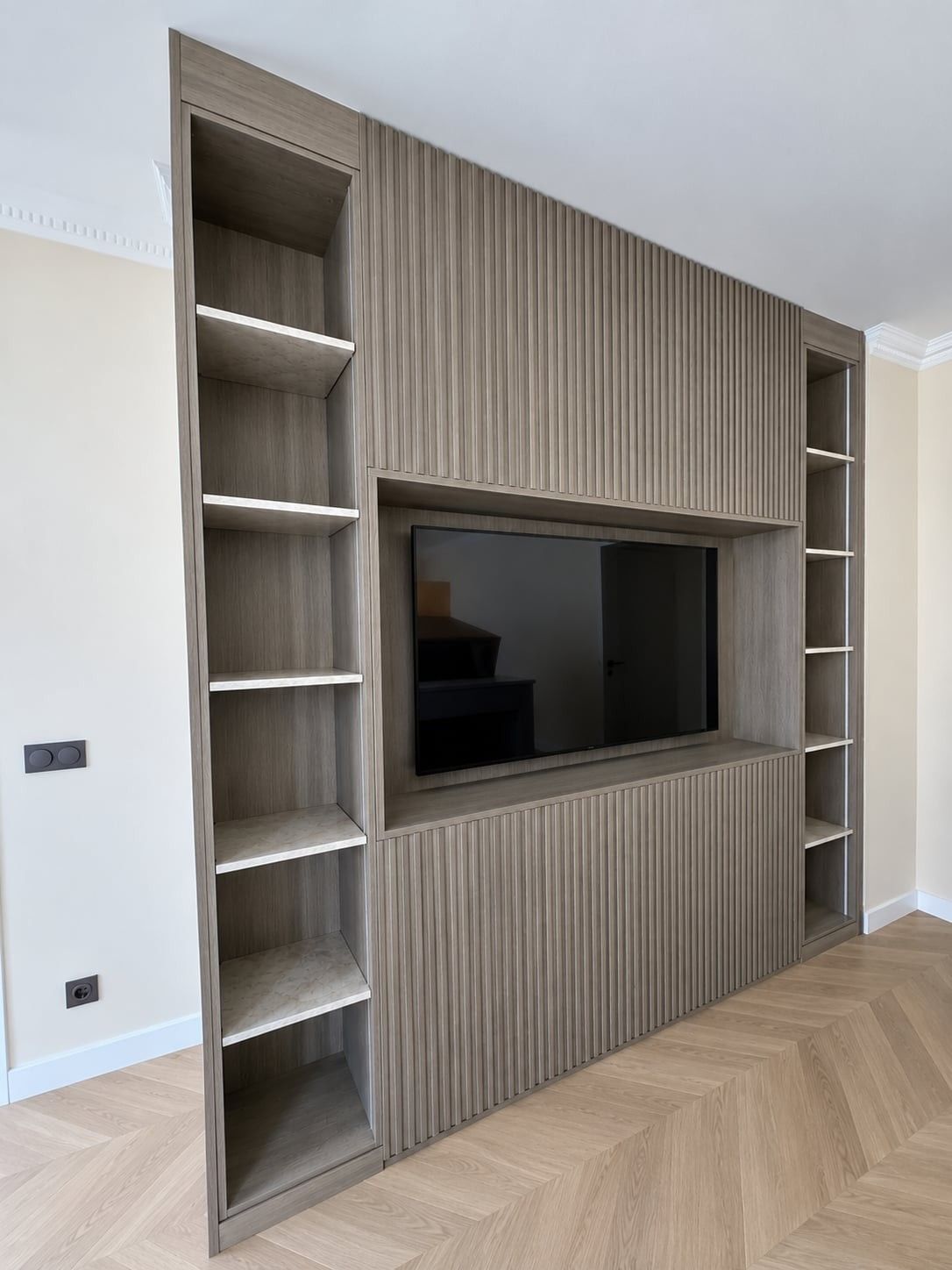 Meuble TV bibliothèque bois gris à façade rainurée et étagères latérales, sur parquet en point de Hongrie