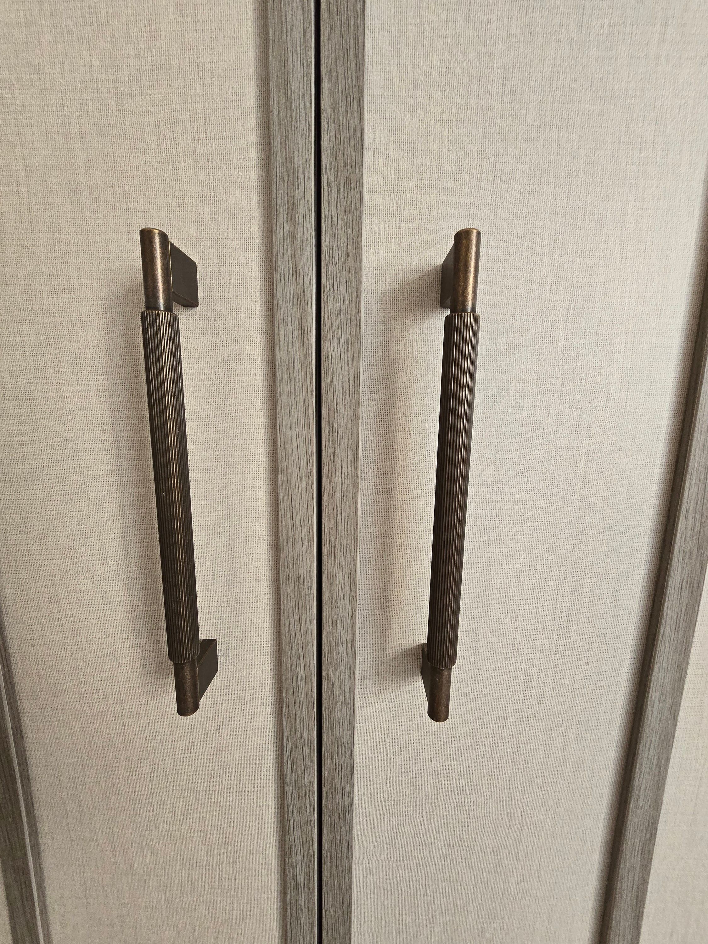 Poignées cannelées finition bronze sur des portes tendues de tissu, aux chants bois gris