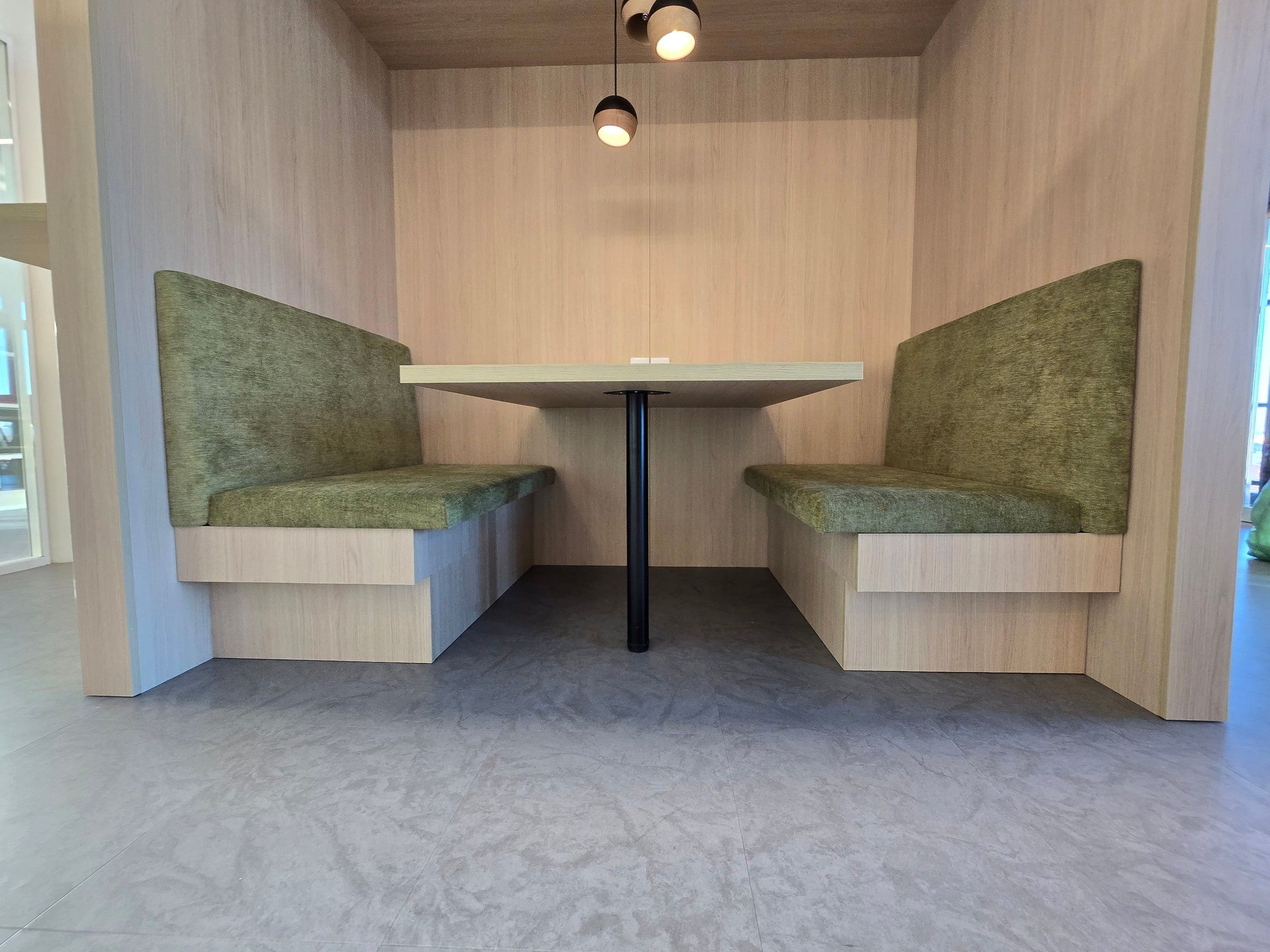Banquettes en tissu vert chiné sur socle en bois, de part et d'autre d'une table sur pied noir