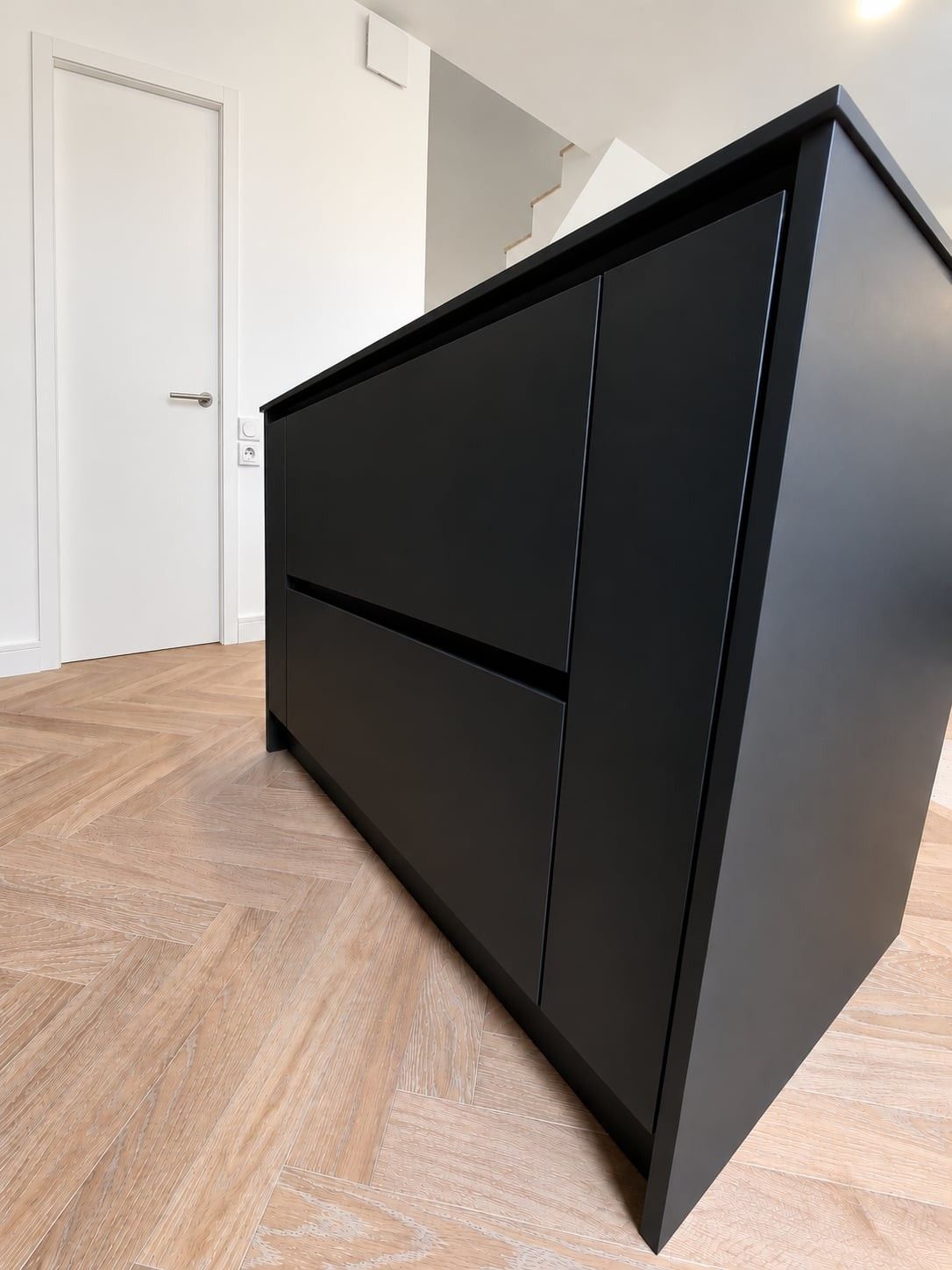Tiroirs sans poignée de l'îlot noir mat, vus en contre-plongée sur le parquet en point de Hongrie