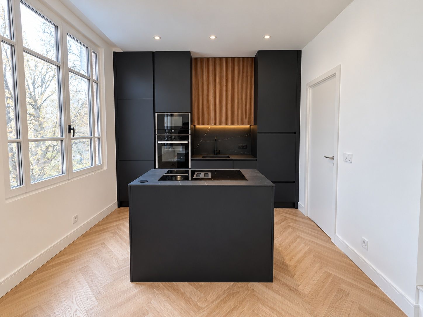 Cuisine noire avec îlot central et niche en bois, sol en parquet à bâtons rompus