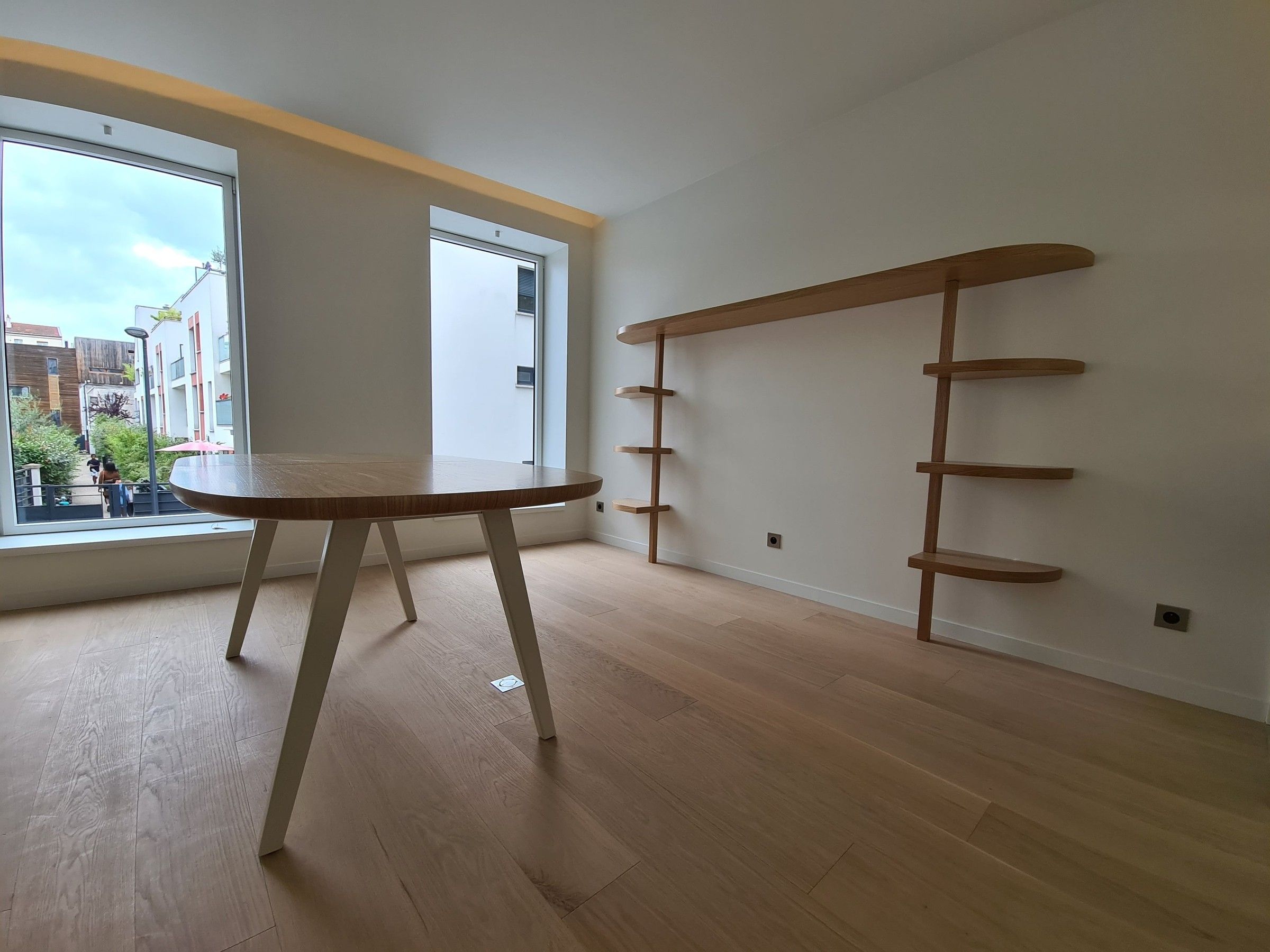 Étagère murale en chêne à tablettes arrondies, à côté d'une table ovale près des fenêtres