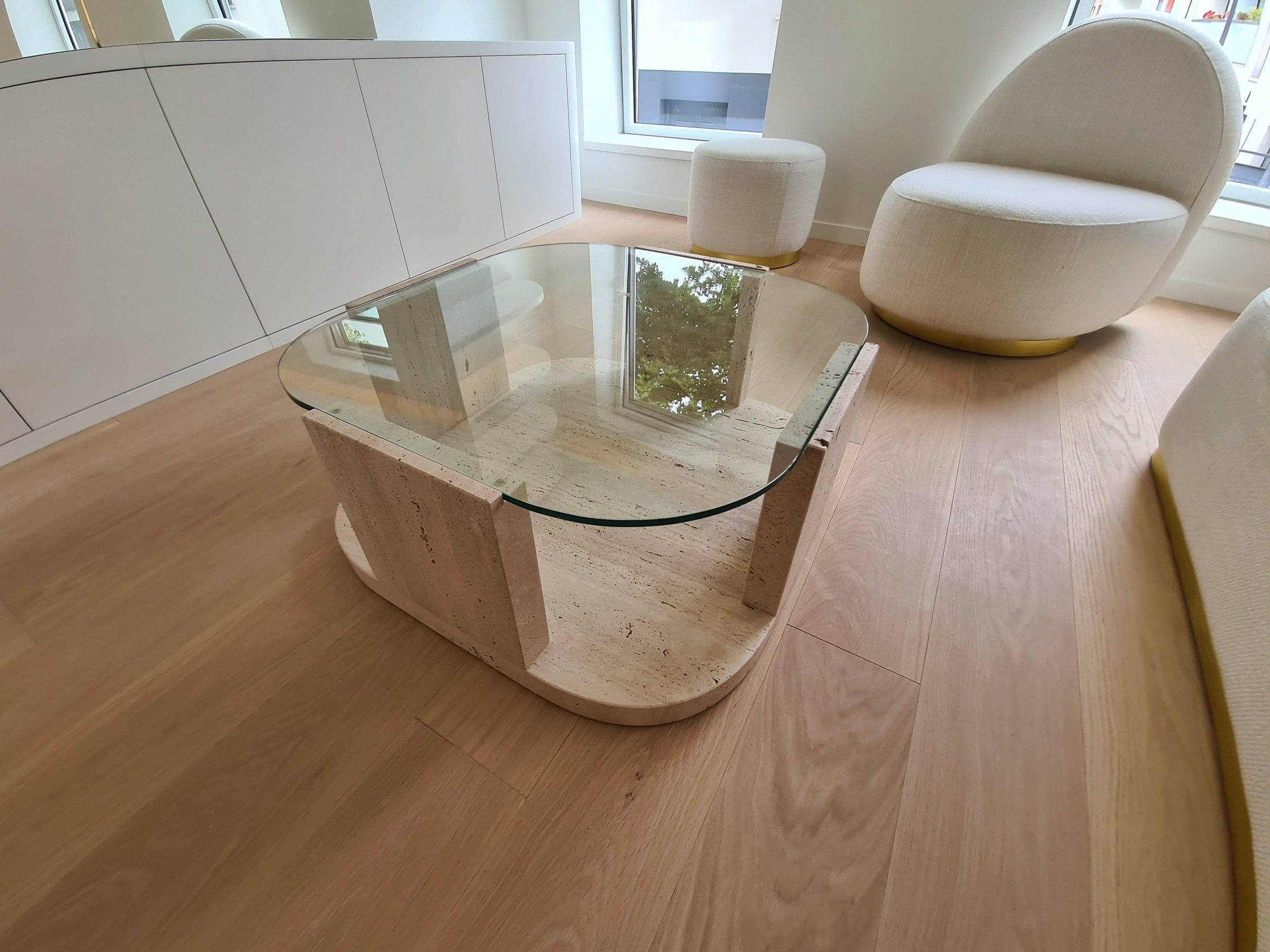 Table basse en travertin aux angles arrondis et plateau en verre, entre fauteuil et meuble bas
