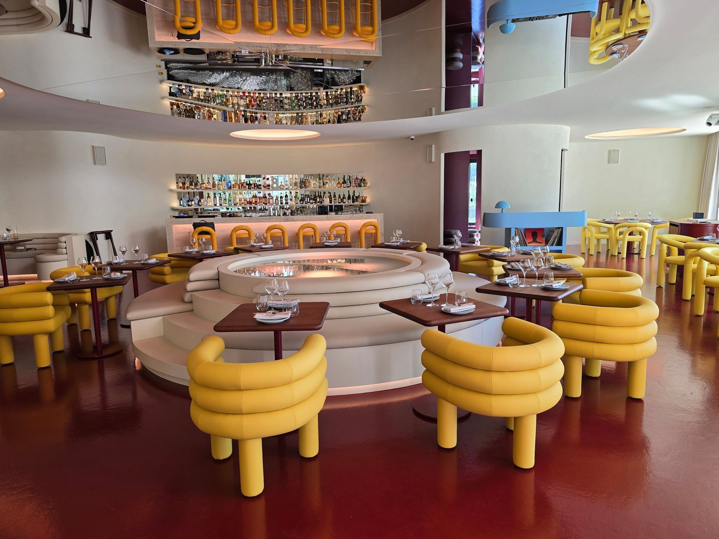 Salle du restaurant Poissonchat : banquette circulaire autour d'un plateau lumineux, fauteuils jaunes et bar en fond